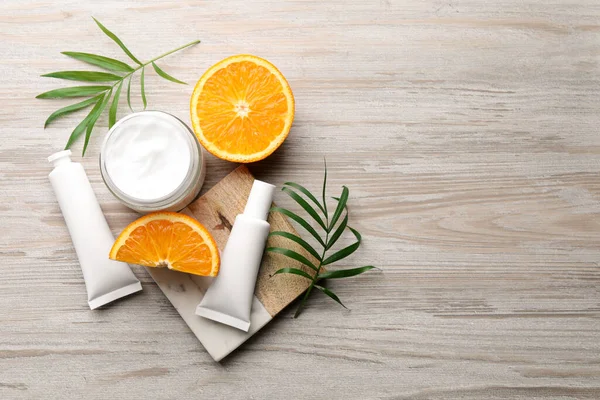 Different hand care cosmetic products, orange and green leaves on white wooden table, flat lay. Space for text