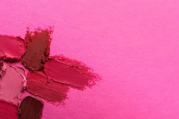 Smears of beautiful lipsticks on pink background, top view. Space for text