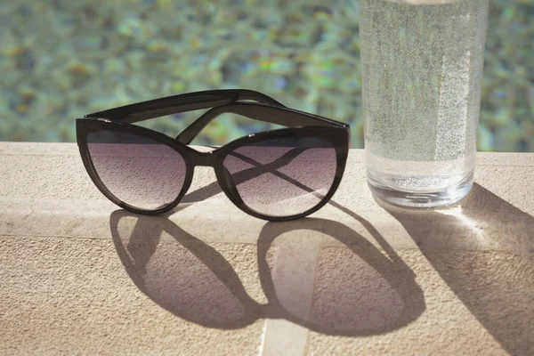 Óculos Sol Elegantes Vidro Água Perto Piscina Exterior Dia Ensolarado — Fotografia de Stock