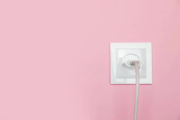 Charger adapter plugged into power socket on pink wall, space for text. Electrical supply