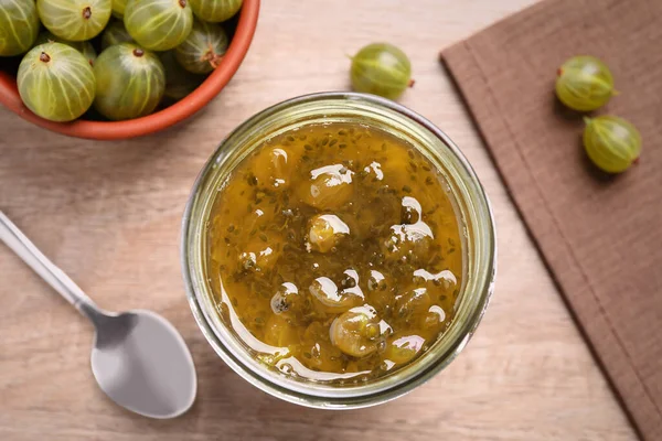 stock image Jar of delicious gooseberry jam and fresh berries on wooden table, flat lay