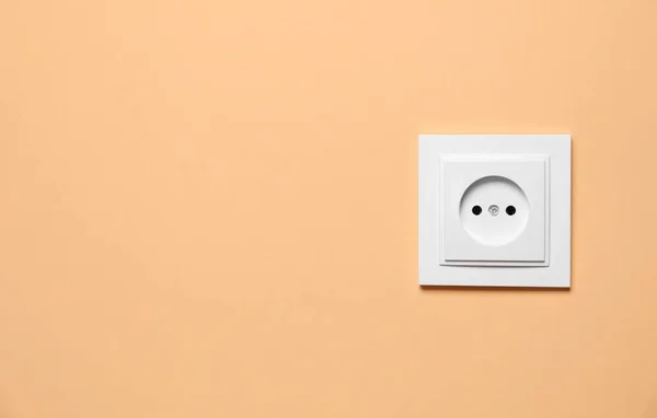 Power socket on pale orange wall, space for text. Electrical supply
