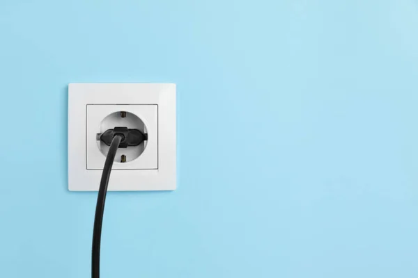 Power socket with inserted plug on light blue wall, space for text. Electrical supply