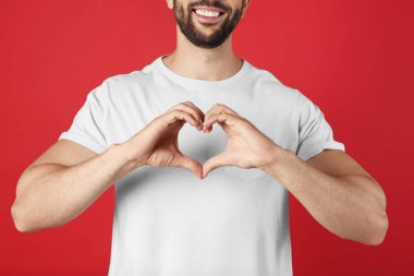 Kırmızı arka planda elleri olan adam kalp yapıyor, yakın plan.