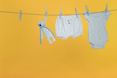 Bebek kıyafetleri ve ayı oyuncağı turuncu arka planda çamaşır ipinde kuruyor.