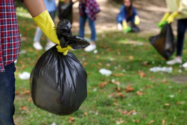 Parkta çöp dolu plastik poşet tutan adam, yakın plan. Metin için boşluk