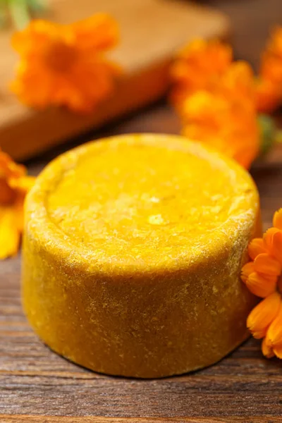 Yellow solid shampoo bar and flowers on wooden table, closeup. Hair care