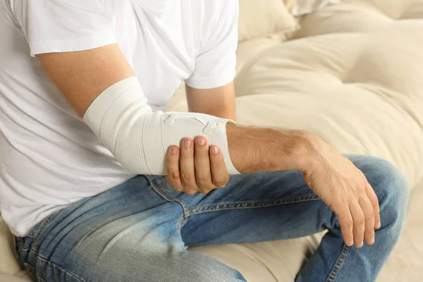 Man with arm wrapped in medical bandage on sofa, closeup
