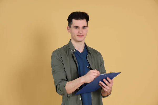 Handsome Young Man Writing Clipboard Beige Background — Zdjęcie stockowe