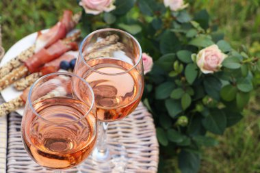 Flowers near glasses of delicious rose wine and food on picnic basket outdoors, closeup