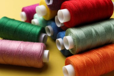 Sarı arkaplanda farklı renkli dikiş iplikleri, yakın plan