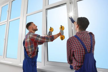 Workers using suction lifters during plastic window installation indoors