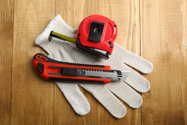 Utility knife, measuring tape and glove on wooden table, top view