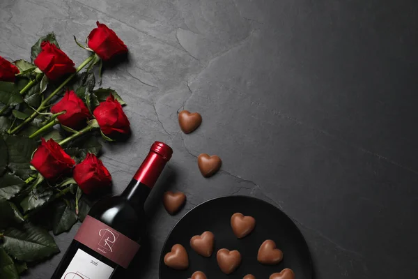 一壶红葡萄酒 美丽的玫瑰和心形巧克力糖果放在黑桌上 平平的躺着 案文的篇幅 — 图库照片