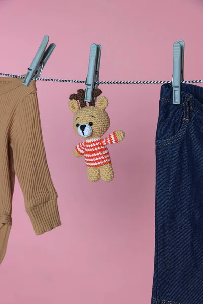 不同的婴儿服装和熊玩具在洗衣店的晾晒线上粉色背景 — 图库照片