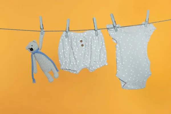 Bebek Kıyafetleri Ayı Oyuncağı Turuncu Arka Planda Çamaşır Ipinde Kuruyor — Stok fotoğraf