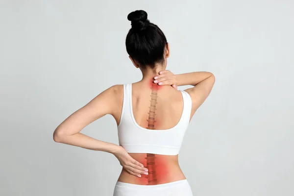 光の背景で背中の痛みに苦しむ女性 — ストック写真