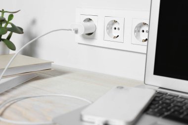 Laptop ve akıllı telefon ahşap masada şarj oluyor, yakın plan.