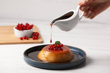 Kadın, kırmızı üzümlü lezzetli pudinge karamel döküyor ve beyaz ahşap masaya nane şekeri döküyor. Yakın plan.