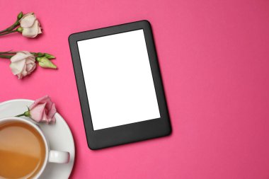 Bir fincan çay ve pembe arka planda çiçekli e-kitap okuyucusu. Metin için boşluk