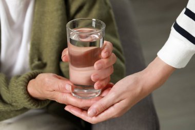 Caregiver giving water to elderly woman at home, closeup