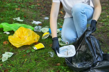 Yeşil çimlerde çöp toplayan plastik çantalı kadın, yakın plan.