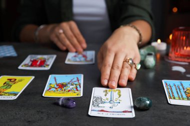 Geleceği tahmin eden falcı, kapalı alandaki gri masada tarot kartlarının yayılmasını bekliyor.