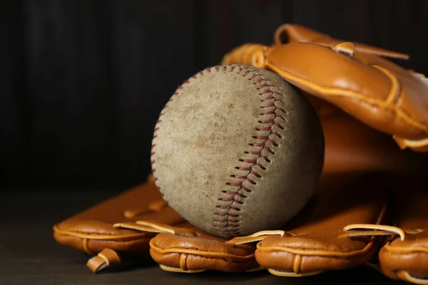 Leather baseball glove with old worn ball on wooden table, closeup