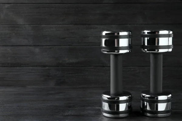 Two metal dumbbells on black wooden table. Space for text