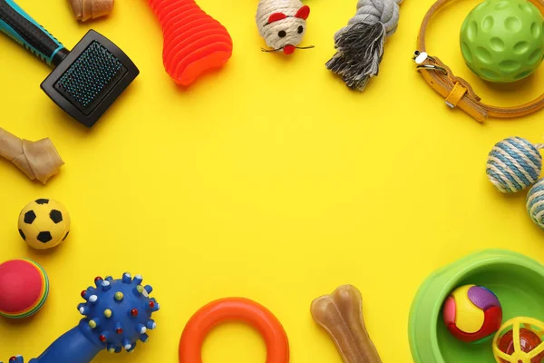 Frame made with pet toys and feeding bowl on yellow background, flat lay. Space for text