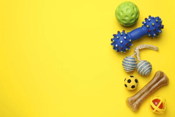 Pet toys and dog treat on yellow background, flat lay. Space for text