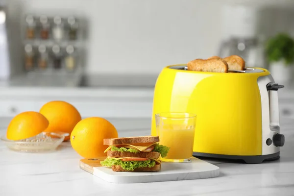 黄色烤面包机 烤面包片 三明治 橙子和果汁放在白色大理石桌上 — 图库照片