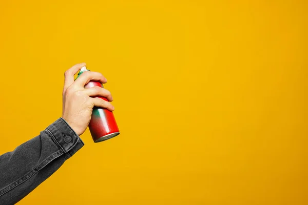Man holding can of spray paint on yellow background, closeup. Space for text