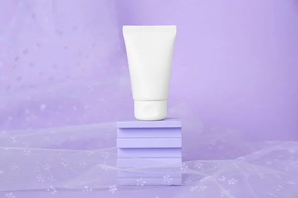 Tube of hand cream and fabric on violet background