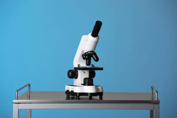 Modern microscope on metal table against blue background