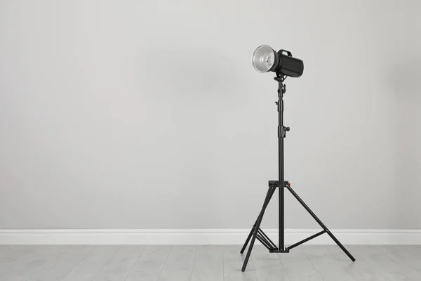 工作室闪光灯与反射镜在三脚架靠近灰色墙壁的房间 空间为文字 专业摄影师设备 — 图库照片