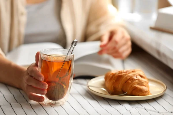 stock image Woman with glass cup of tasty aromatic tea reading book at table, closeup