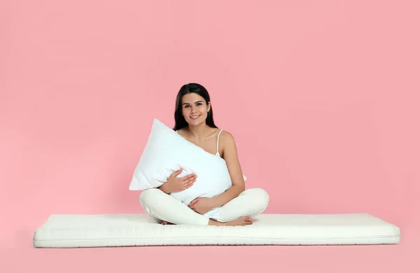 Jovem Mulher Sentada Colchão Macio Segurando Travesseiro Contra Fundo Rosa — Fotografia de Stock