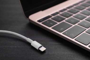 USB kablosu, şimşek konnektörü ve dizüstü bilgisayarı siyah ahşap masada, yakın plan.