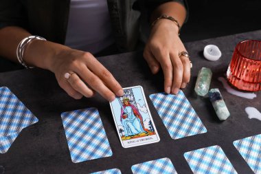 Falcı, gri masada tarot kartlarının yayılması üzerine geleceği tahmin ediyor, yakın plan.