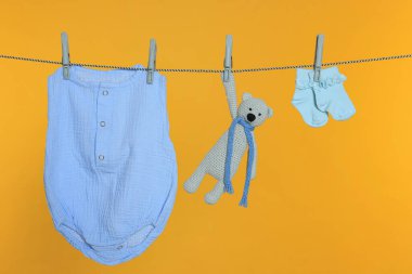 Bebek kıyafetleri ve oyuncak çamaşır ipinde turuncu arka planda kuruyor.