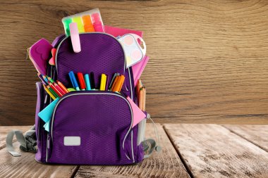 Okul kırtasiyesinin olduğu sırt çantası ahşap arkaplan, metin için boşluk