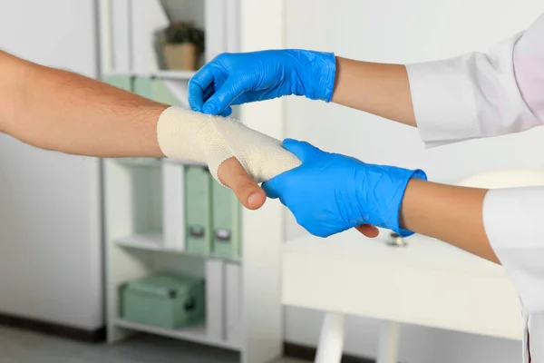 stock image Doctor applying medical bandage onto patient's hand in hospital, closeup