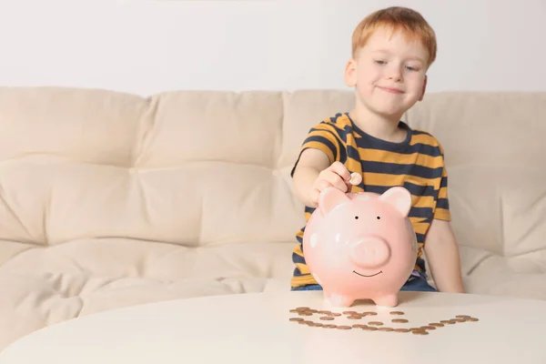 Netter Kleiner Junge Legt Münze Sparschwein Tisch Drinnen Konzentriert Sich — Stockfoto