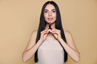 Bej arka planda çıplak ruj tutan güzel makyajlı genç bir kadın.