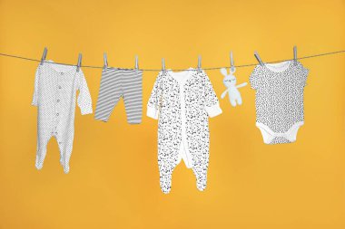 Bebek kıyafetleri ve tavşan oyuncağı turuncu arka planda çamaşır ipinde kuruyor.