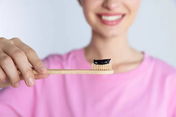 stock image Woman holding brush with charcoal toothpaste on light background, closeup