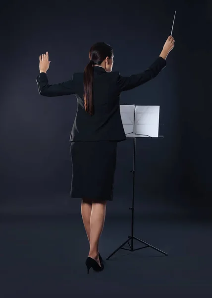 stock image Professional conductor with baton and note stand on dark background, back view