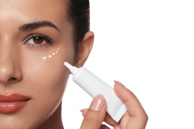 Woman applying cream under eyes on white background, closeup. Skin care