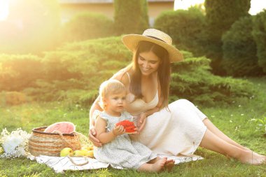 Mother with her baby daughter having picnic in garden on sunny day